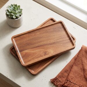 Two brown acacia wood serving trays stacked on rustic table